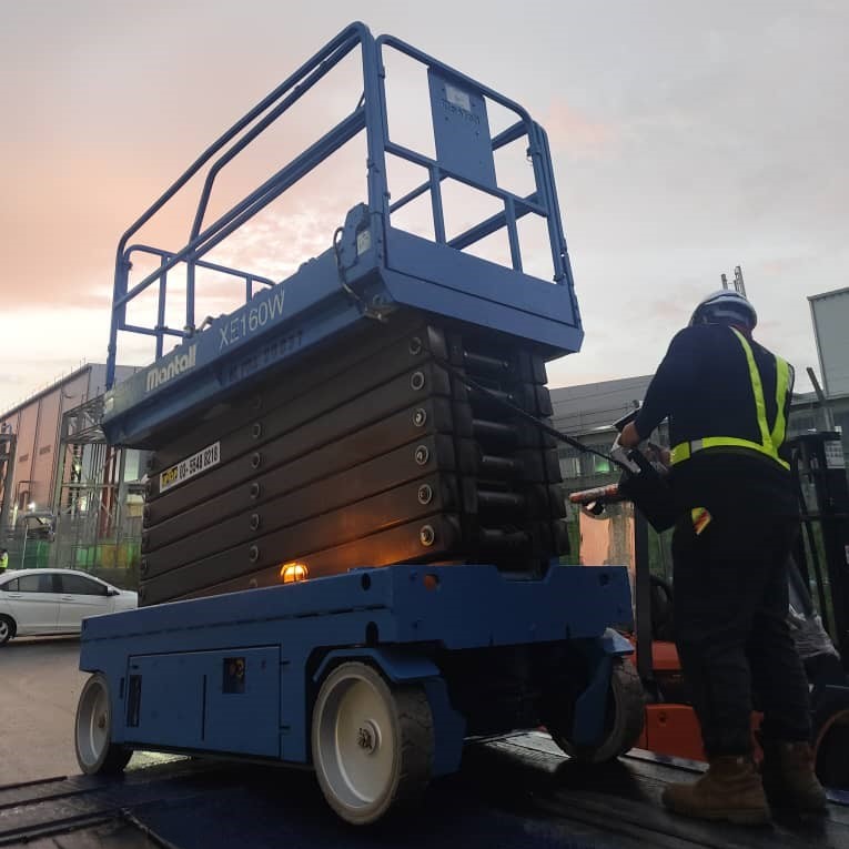Operator with a blue Mantall Scissor Lift MEWP at a worksite.